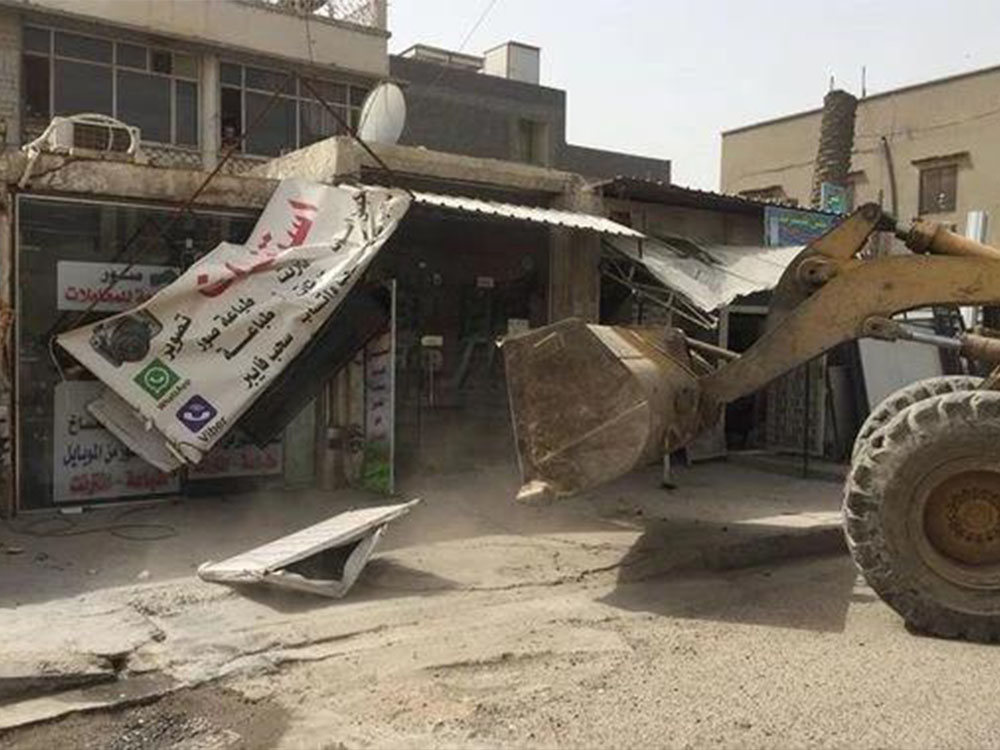كوادر بلدية تنفذ حملة ميدانية لإزالة التجاوزات في أحد الأسواق، حيث يجري تحميل المواد المخالفة على مركبة تابعة للبلدية ضمن إجراءات تنظيم الأرصفة والشوارع.