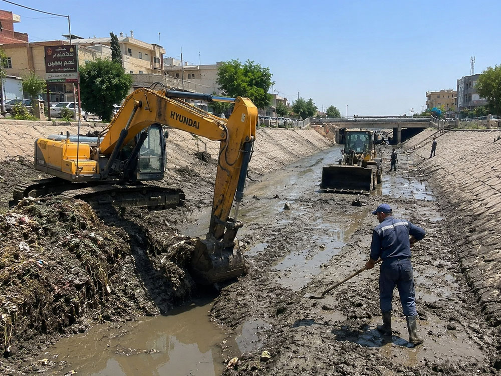 كوادر وآليات مجاري نينوى تنفذ أعمال تنظيف وكري وادي الجديدة في الموصل، مع إزالة الأطيان والنفايات من مجرى الوادي.