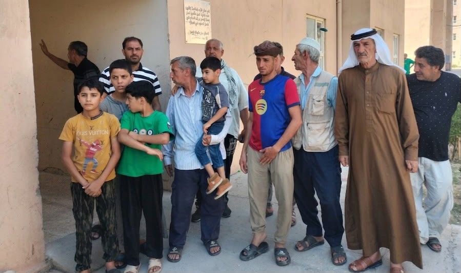 مجموعة من سكان مجمع باب سنجار السكني في الجانب الأيمن من مدينة الموصل، بينهم رجال وأطفال، يقفون أمام إحدى البنايات السكنية خلال وقفة احتجاجية اعتراضًا على قرارات إخلاء الشقق.