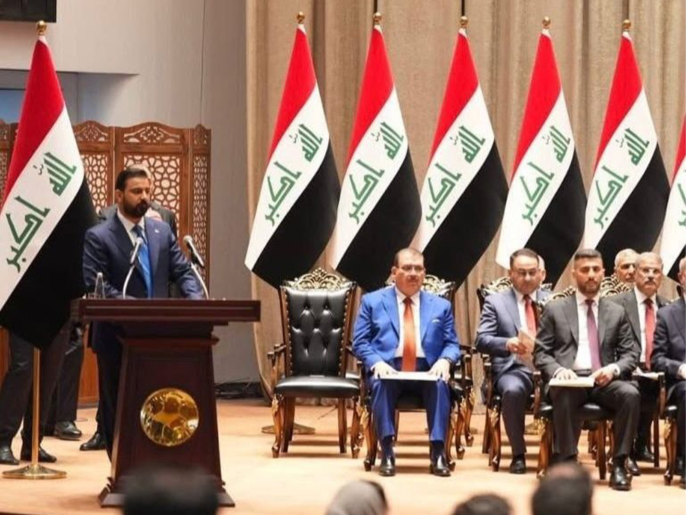صورة لاجتماع أو مناسبة رسمية في العراق، يظهر فيها عدد من المسؤولين والنواب على منصة تتزين بالأعلام العراقية، علی فالح الزیدی يقف خلف المنصة لإلقاء كلمة أمام الحضور.