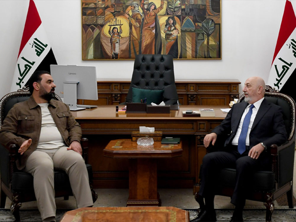 يجلس مسؤولان عراقيان في اجتماع رسمي داخل مكتب حكومي، يتبادلان الحديث وهما يجلسان على مقعدين متقابلين، وتظهر خلفهما رايتا العراق ومكتب رسمي تتوسطه لوحة فنية.