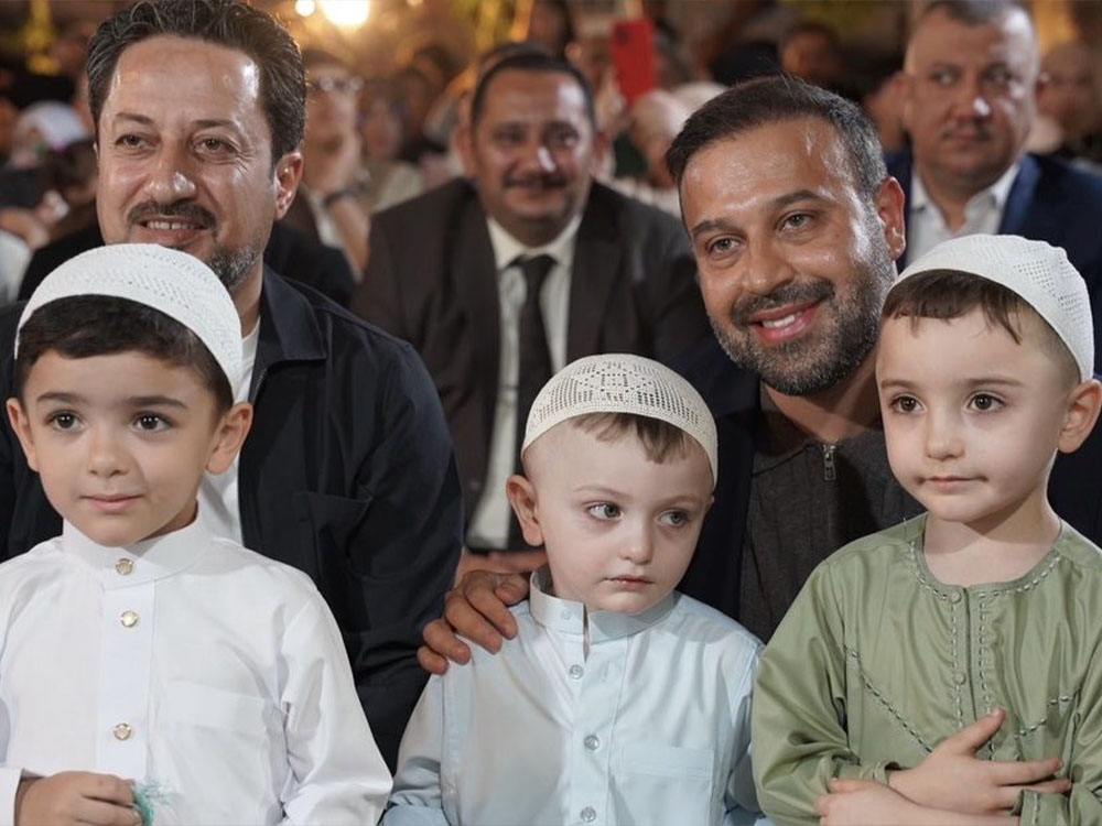 صورة تضم النجیفي وثلاثة أطفال يرتدون طواقي (قبعات) بيضاء وثياباً تقليدية في تجمّع أو احتفالية شعبية، ويبدو على الحضور التبتسم والأجواء الاحتفالية.