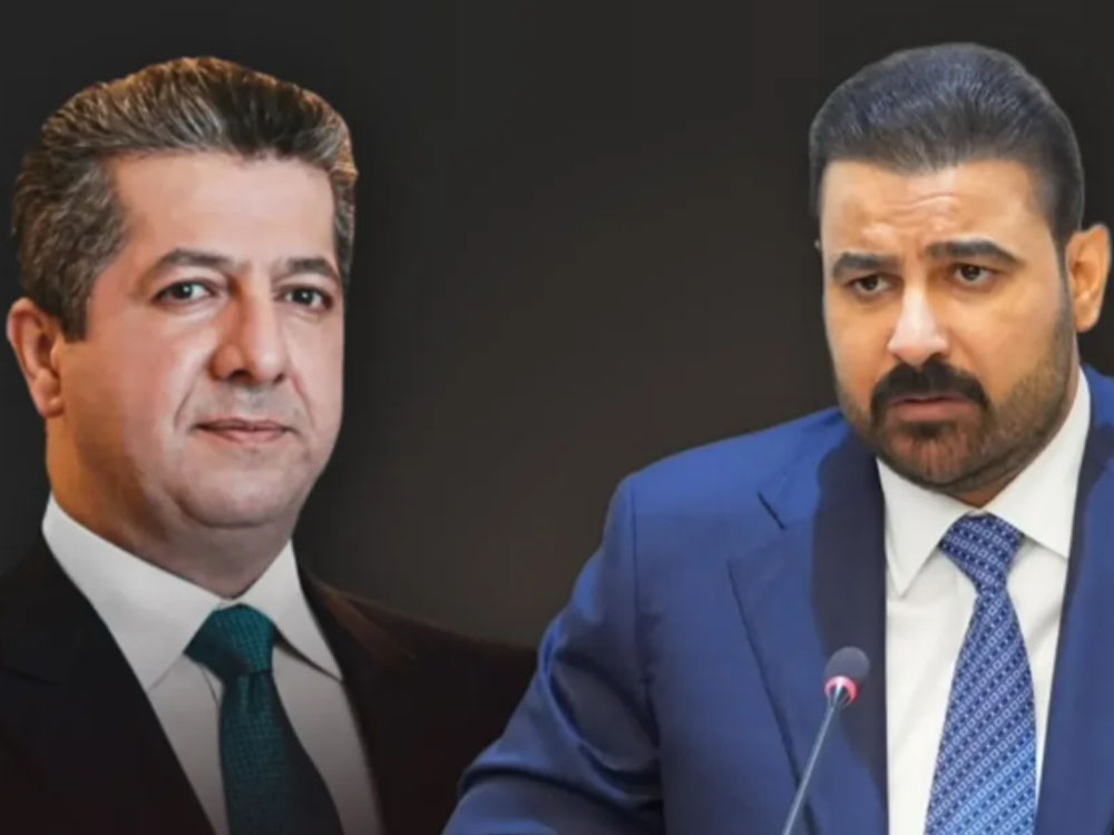 "صورة مركبة تجمع بين رئيس حكومة إقليم كردستان مسرور بارزاني (على اليسار) ببدلة سوداء وربطة عنق خضراء داكنة، والأمين العام لكتائب سيد الشهداء أبو آلاء الولائي (على اليمين) ببدلة كحلية وربطة عنق زرقاء ويتحدث أمام ميكروفون، على خلفية داكنة."