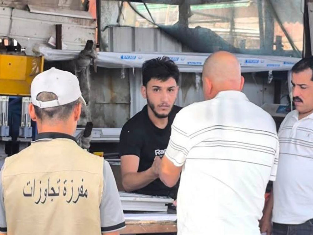 عنصر من مفرزة التجاوزات يرتدي سترة مخصصة يقف أمام أحد أصحاب المحال التجارية أثناء توجيه إنذار له في الموصل.