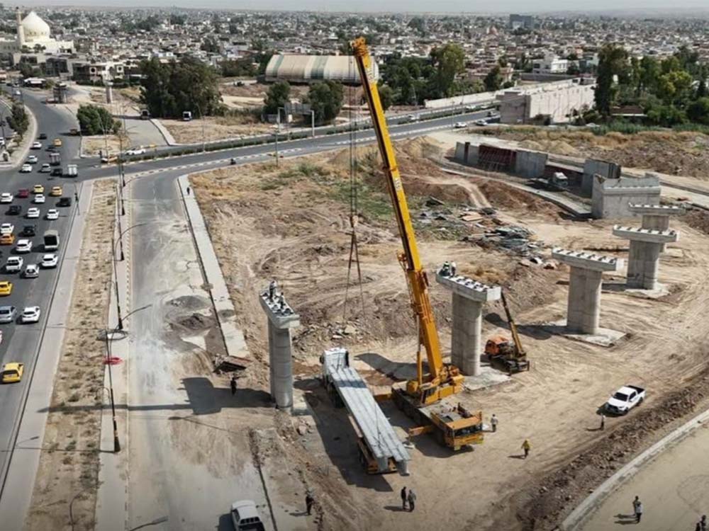 رافعة إنشائية تعمل على تركيب روافد الجسر الرئيس ضمن مشروع تقاطع الصابرين المجسر في مدينة الموصل، مع ظهور الأعمدة الخرسانية وأعمال التنفيذ الجارية في الموقع.