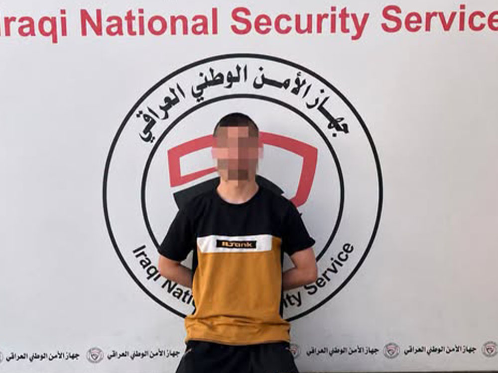 متهم بوجه مموّه يجثو أمام شعار جهاز الأمن الوطني العراقي، عقب إلقاء القبض عليه في محافظة نينوى.