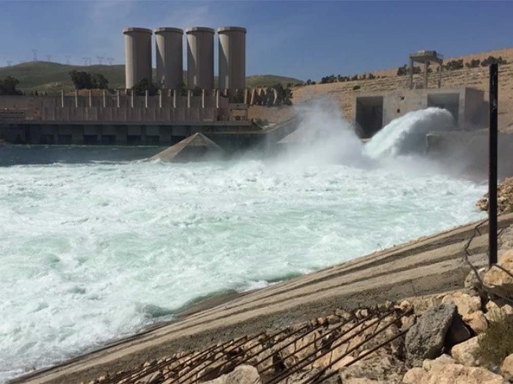 مشهد لتدفق المياه من بوابات سد الموصل إلى مجرى نهر دجلة، مع ظهور منشآت السد والمنشآت الخرسانية المحيطة به شمال مدينة الموصل.
