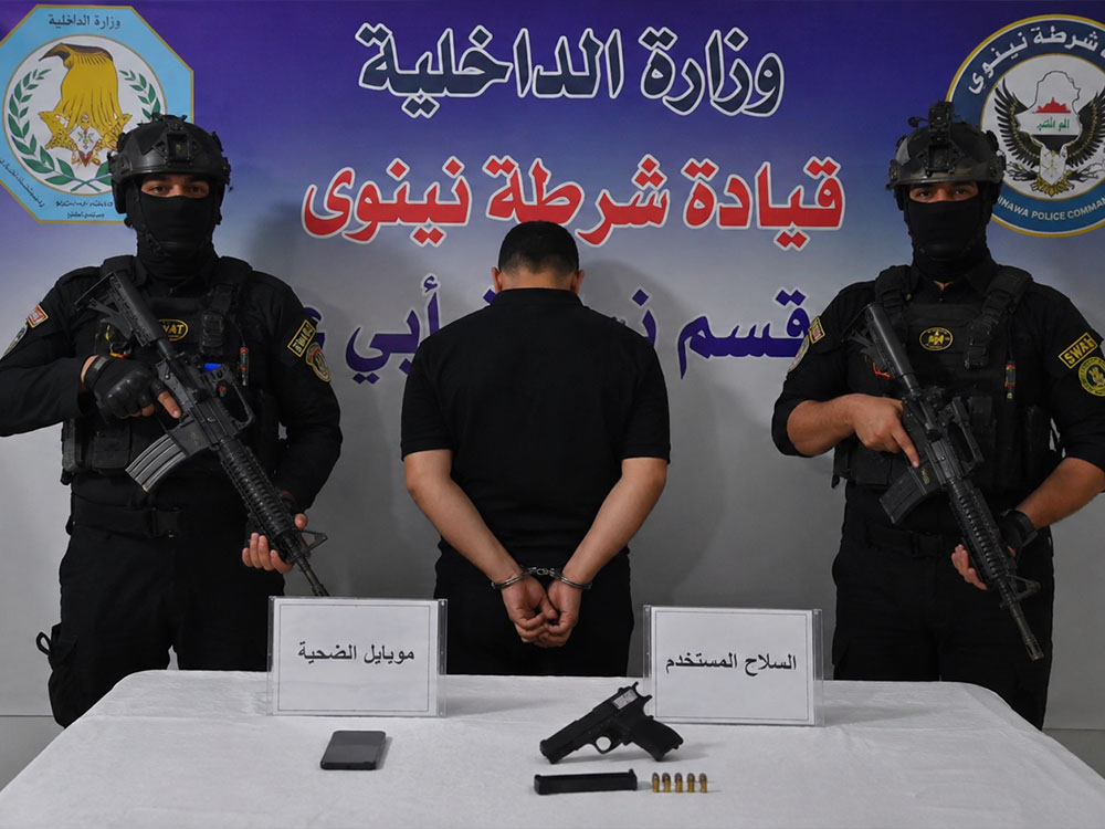 قوات من شرطة نينوى تقف إلى جانب متهم مكبّل الأيدي خلال عرض نتائج التحقيق في جريمة قتل، مع ضبط السلاح المستخدم وهاتف المجني عليه.