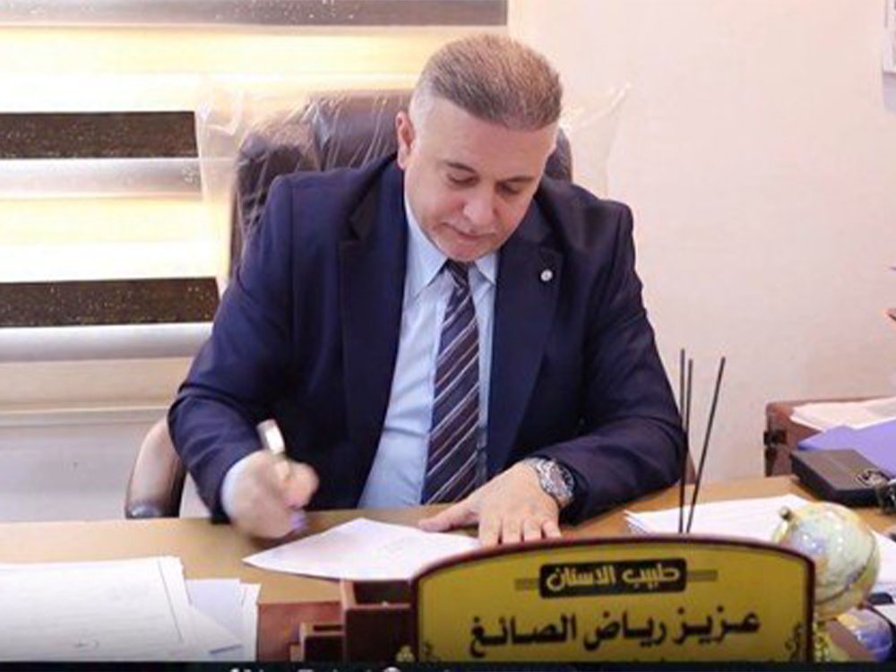 مدير شعبة الرقابة الصحية في نينوى عزيز رياض الصائغ يجلس خلف مكتبه أثناء توقيعه على عدد من الوثائق الرسمية.