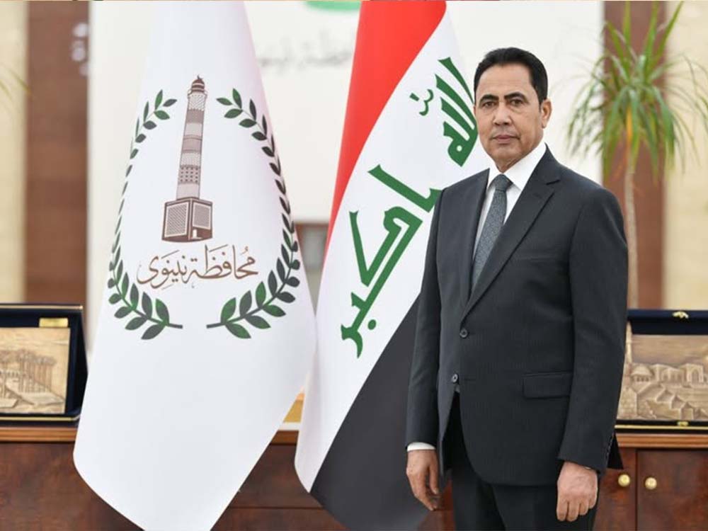 محافظ نينوى عبد القادر الدخيل يقف أمام العلم العراقي وعلم محافظة نينوى