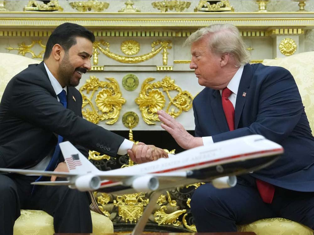 الرئيس الأميركي دونالد ترمب يصافح مسؤولاً عراقياً خلال لقاء في البيت الأبيض، وأمامهما نموذج لطائرة، في مشهد يعكس العلاقات العراقية الأميركية.