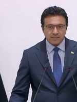 المتحدث باسم الحكومة العراقية حيدر العبودي يقف أمام منصة خلال مؤتمر رسمي، وخلفه العلم العراقي.