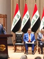 صورة لاجتماع أو مناسبة رسمية في العراق، يظهر فيها عدد من المسؤولين والنواب على منصة تتزين بالأعلام العراقية، علی فالح الزیدی يقف خلف المنصة لإلقاء كلمة أمام الحضور.